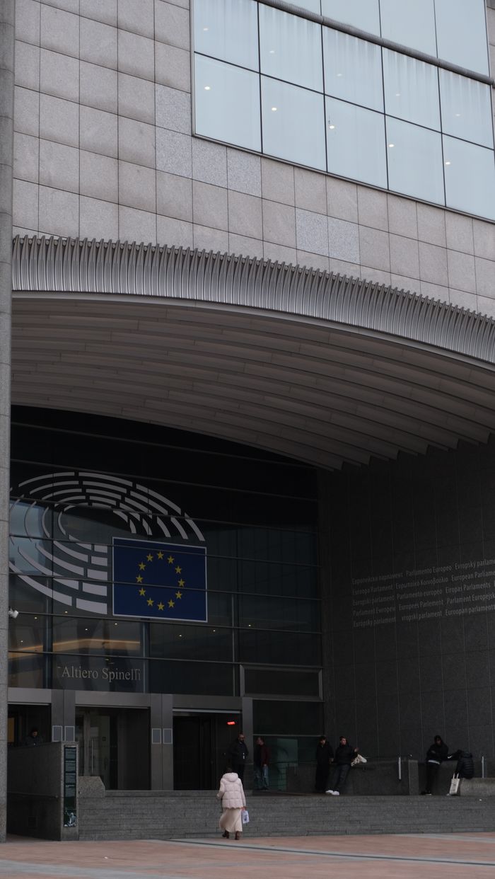 our-story Entrance of European Parliament building in Brussels showcasing modern architecture and EU flag.